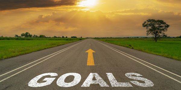 Road with an arrow and the word 'GOALS' painted, leading to a bright horizon.