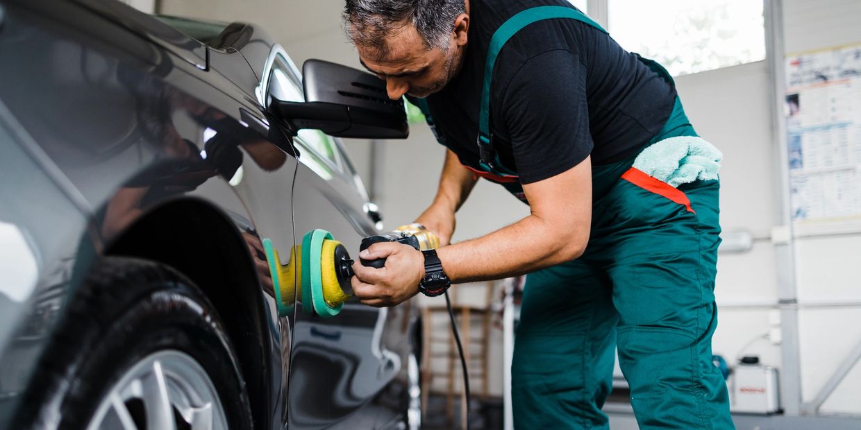 Man polishing a black car with a buffer machine in a garage.