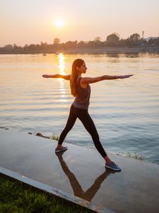 Woman practicing yoga by the water at sunrise.