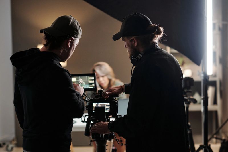Back view of two young men standing in front of camer aand using steadicam while shooting new commercial with female model