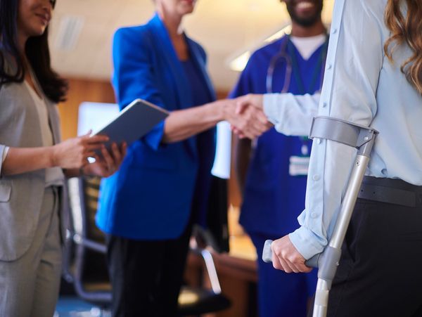 People shaking hands in a professional setting with a person on crutches.