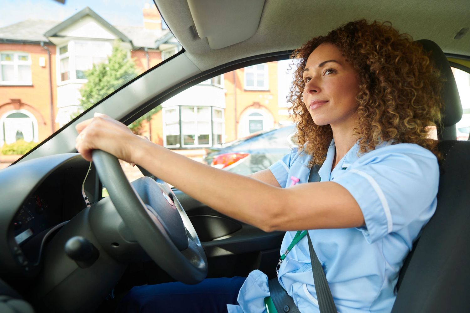 Nurse in blue uniform driving a car with a focused expression.