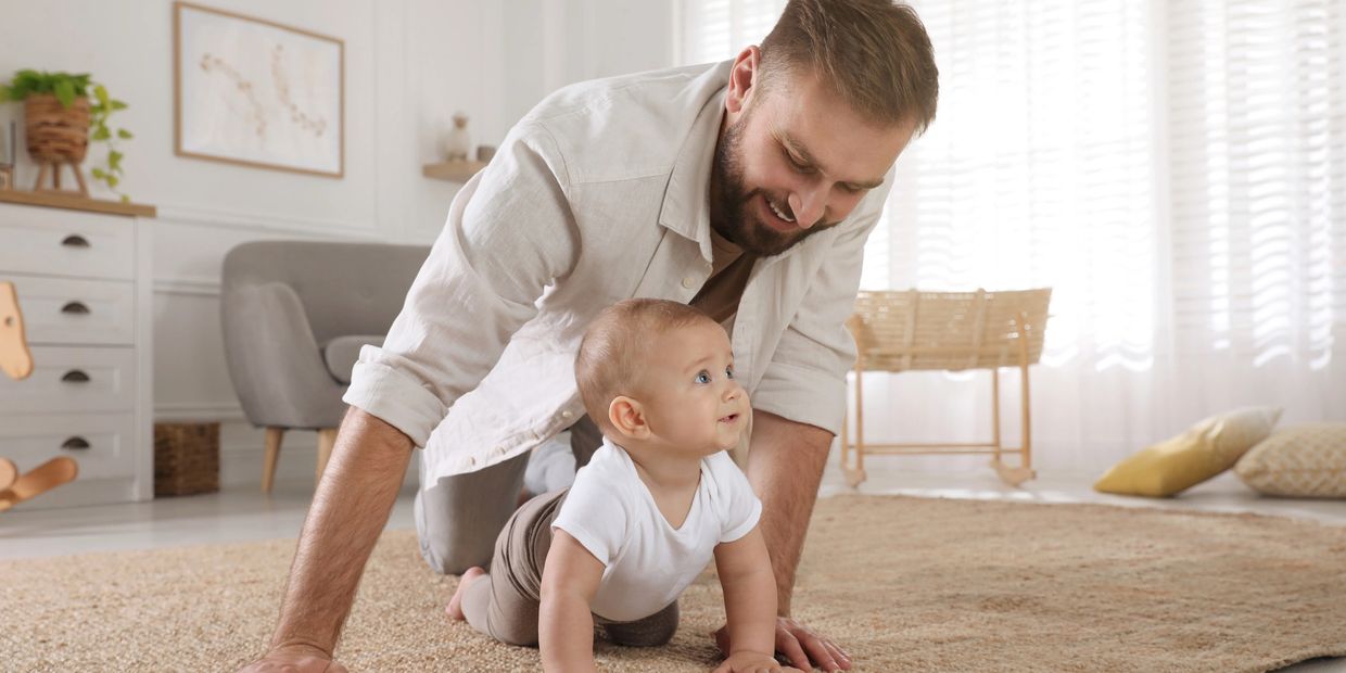 Father watching baby crawl on clean living room floor in a bright, tidy home