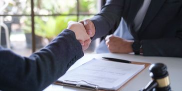 Two professionals shaking hands over a legal document and gavel.