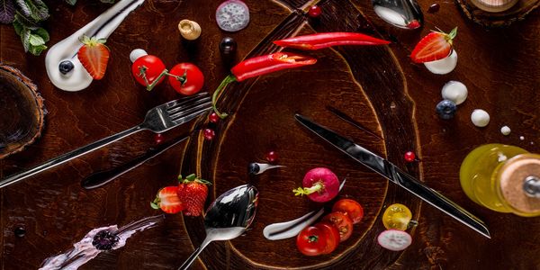Artistic arrangement of fruits, vegetables, and utensils on a wooden surface.