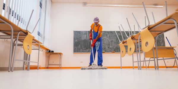 Custodian mops the floor in an empty classroom with chairs on desks.