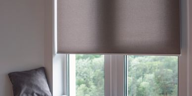 Cozy window nook with grey cushion and pillow under a partially lowered blind.