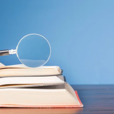 Magnifying glass resting on stacked open books against a blue background.