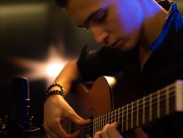 Young man playing acoustic guitar in a dimly lit room.