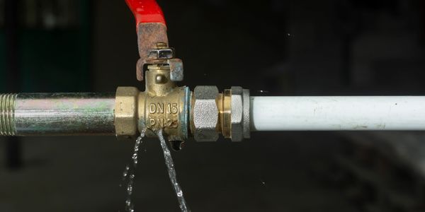 Close-up of a leaking water shutoff valve dripping from the connection point, showing a plumbing leak that requires professional leak detection and pipe repair services.