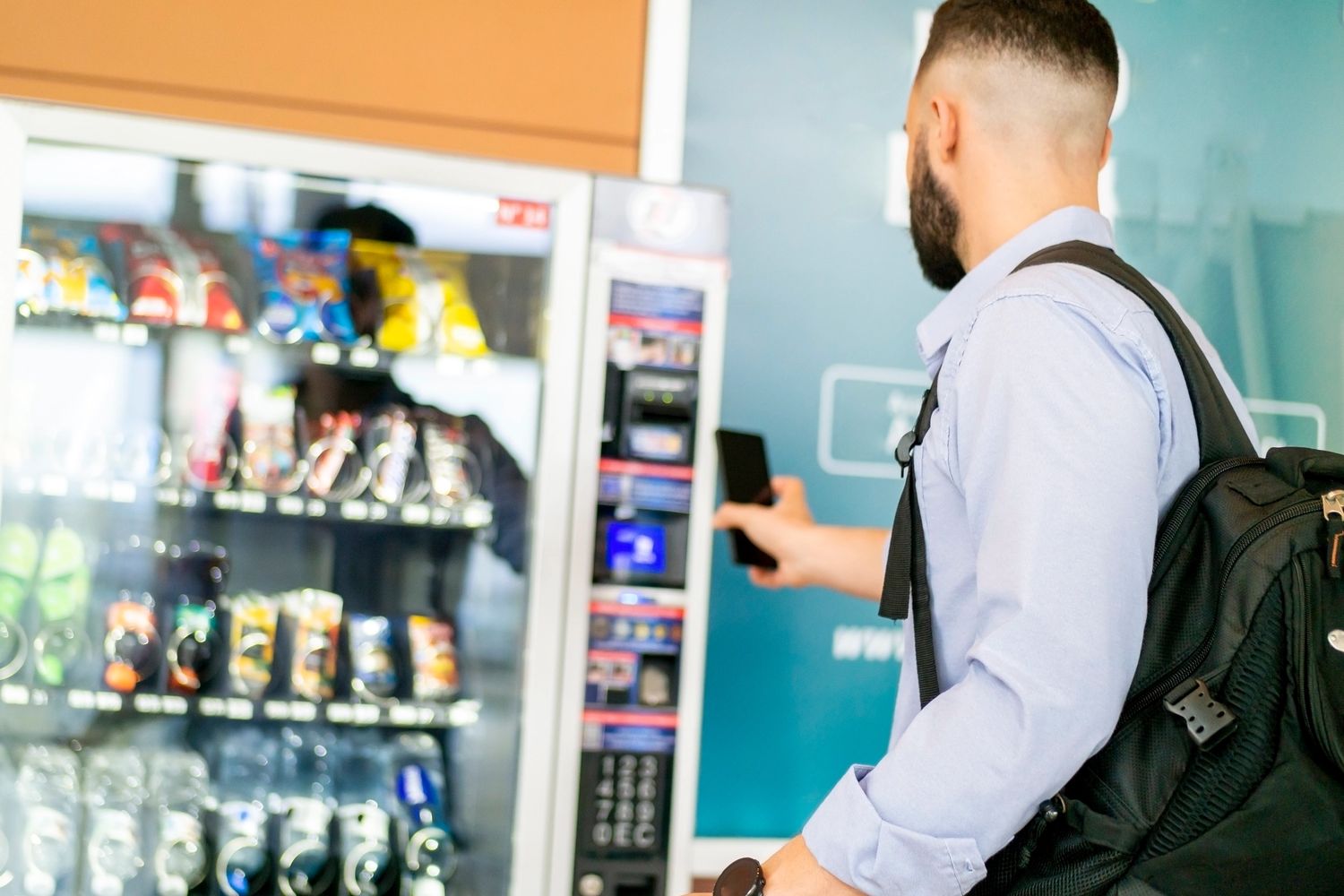 Man using a smartphone to buy snacks from a vending machine.