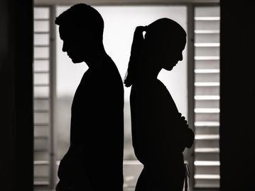 Silhouettes of a man and woman standing back-to-back in disagreement.