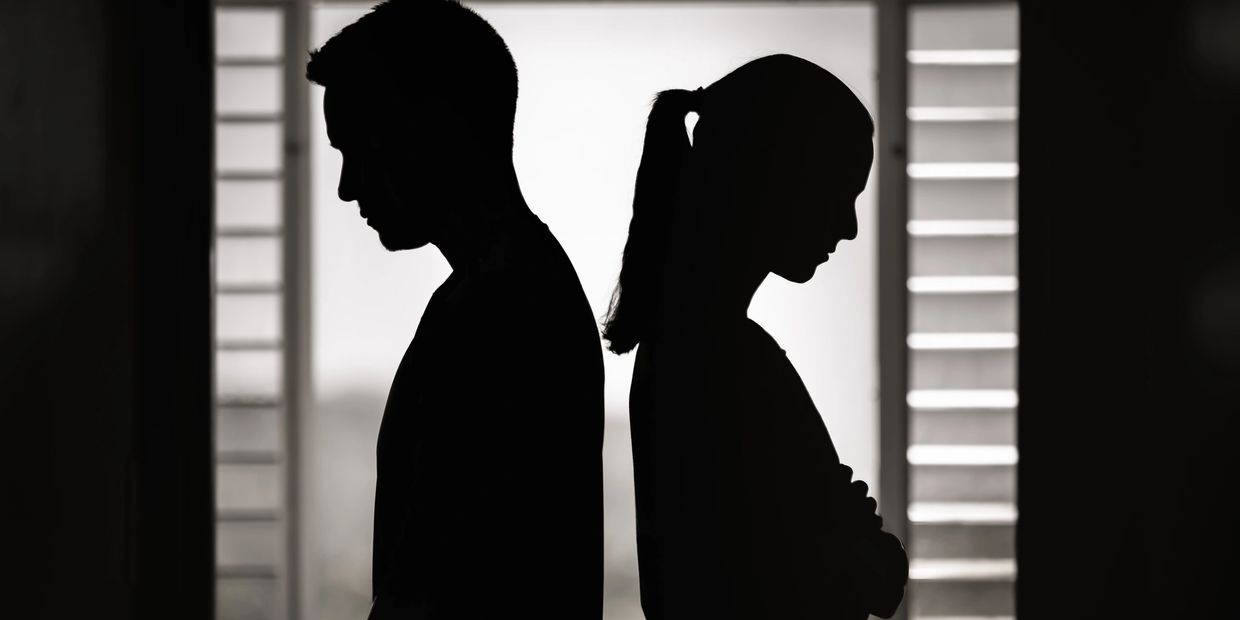 Silhouetted man and woman standing back to back, appearing upset or distant.