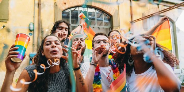 Group of friends celebrating LGBTQ+ pride with rainbow flags and party blowers.