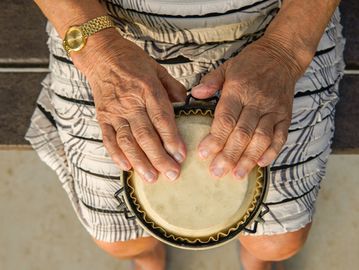 Elderly hands gently playing a small drum.