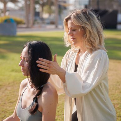 A woman giving a head massage to another woman outdoors.