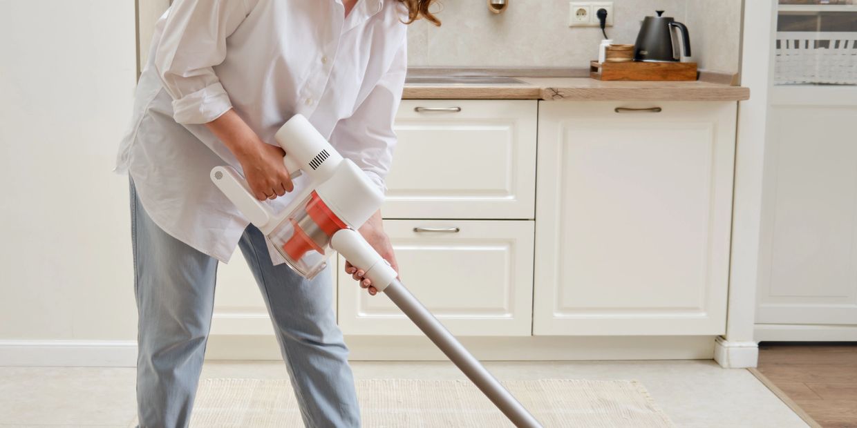 Person vacuuming a light-colored rug in a modern kitchen.