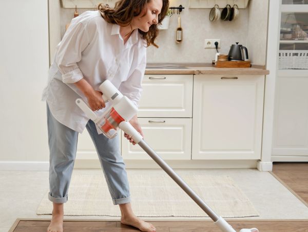 Woman vacuuming wooden floor barefoot in a modern kitchen.