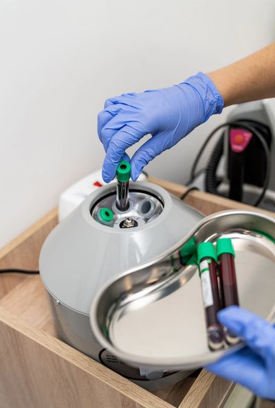 A gloved hand placing a blood sample tube into a centrifuge machine.