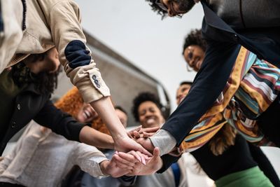 A diverse group of people standing together with their hands joined in the center, symbolizing unity