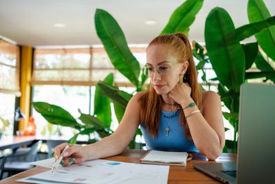 A woman analyzing documents at a desk surrounded by plants.