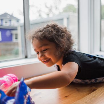 A joyful child playing near a window on a wooden floor.