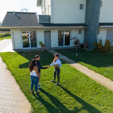 Real estate agent handing keys to a couple outside a modern house.