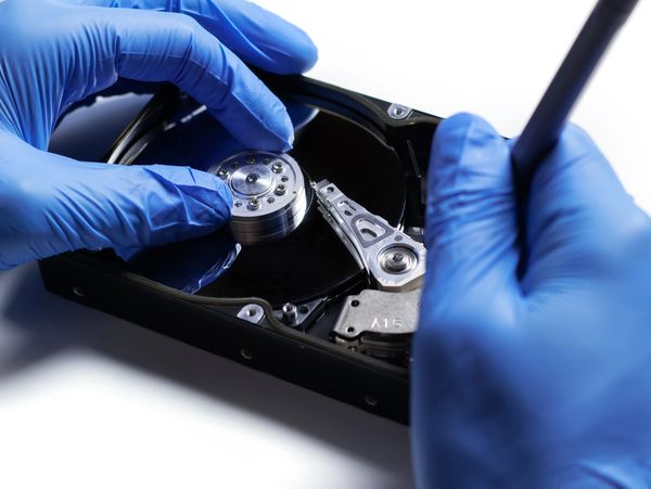 Technician repairing a hard drive with precision tools and blue gloves.