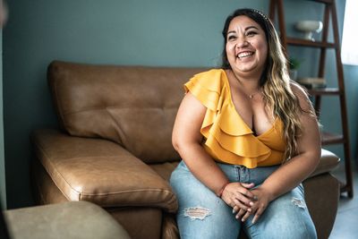 Woman in a yellow top smiling while sitting on a brown couch.