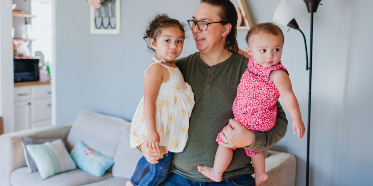 A man holding two young children in a cozy living room.