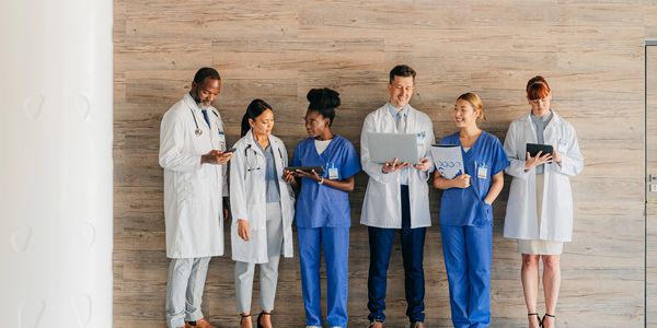 Diverse medical team in scrubs and lab coats using digital devices and documents.