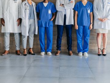 A group of healthcare professionals standing side by side, wearing scrubs and lab coats.