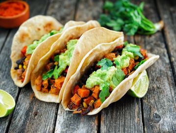 Three tacos filled with vegetables, black beans, and guacamole on a wooden surface.
