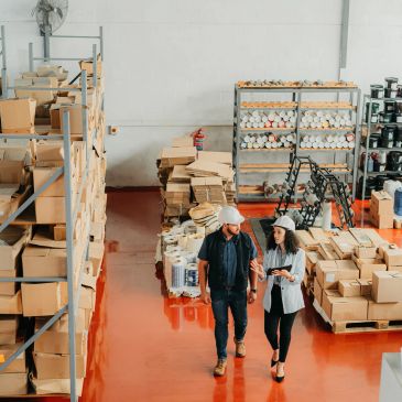 Two workers inspecting inventory in a large warehouse filled with boxes and supplies.