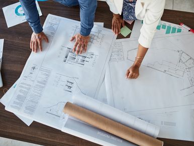 Two people reviewing architectural blueprints on a table.