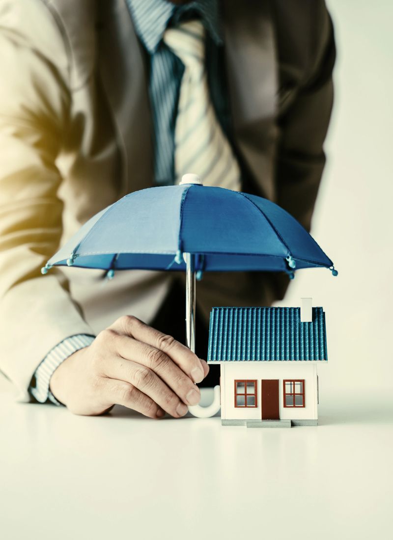 An insurance agent is holding a blue umbrella over a modern house model. Property insurance concept. Protection of housing / house. Security and safety housing insurance Service