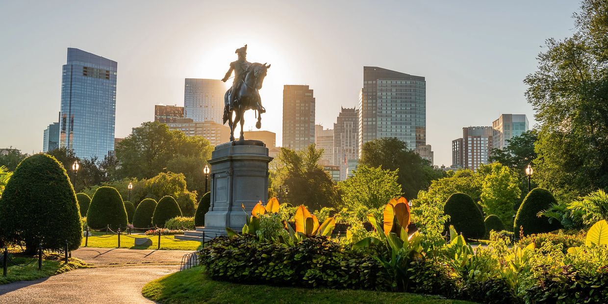 Equestrian statue in a city park with modern skyscrapers.
