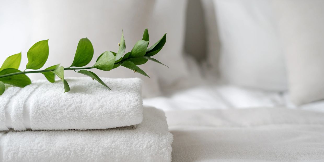 White towels with green leaf on a bed.