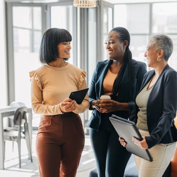 Three women having a discussion in a bright office.
