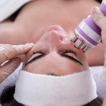 Woman receiving a facial treatment with a handheld device.