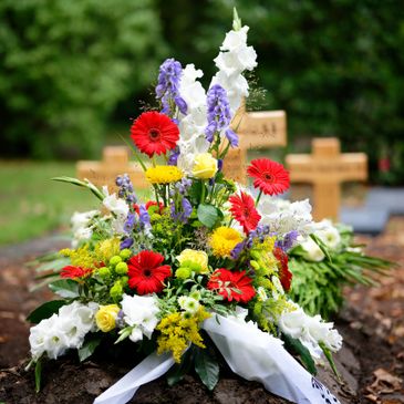 Colorful floral arrangement on a grave with wooden crosses in the background.