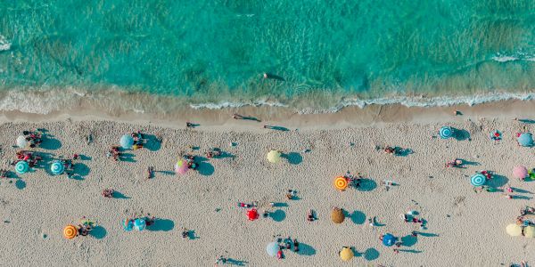 Aerial view of people on a beach with colorful umbrellas.