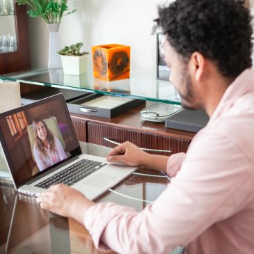 Man video chatting with a woman on a laptop at a glass table.