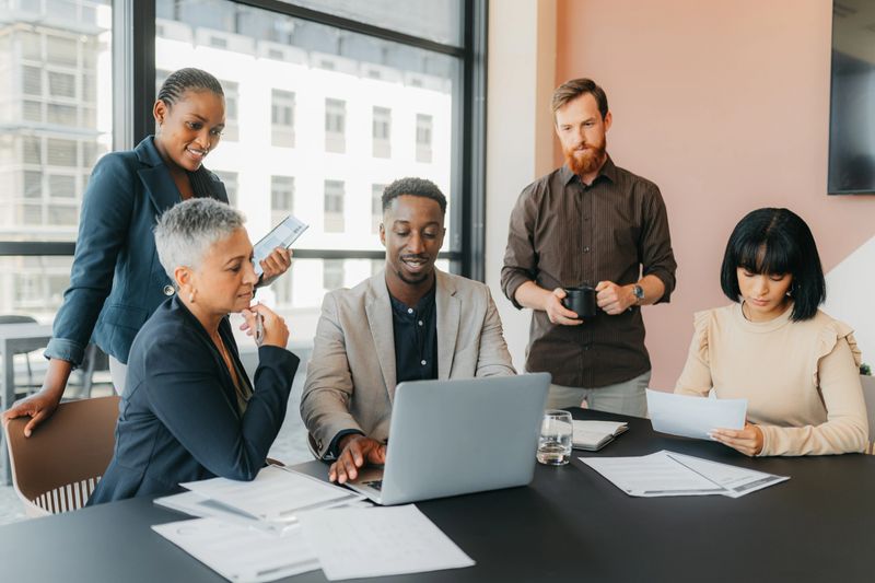 Business people planning marketing strategy on laptop, reading documents for project in meeting and discussion in workshop in office. Team collaboration working in corporate and internet research