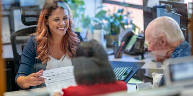 Smiling woman assisting two elderly people at a counter.