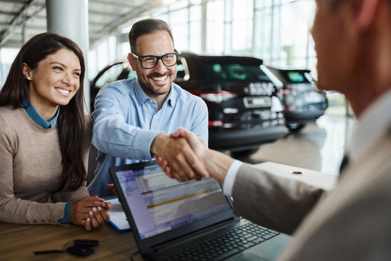 Young happy couple came to a successful agreement with car salesman during a meeting in a showroom.