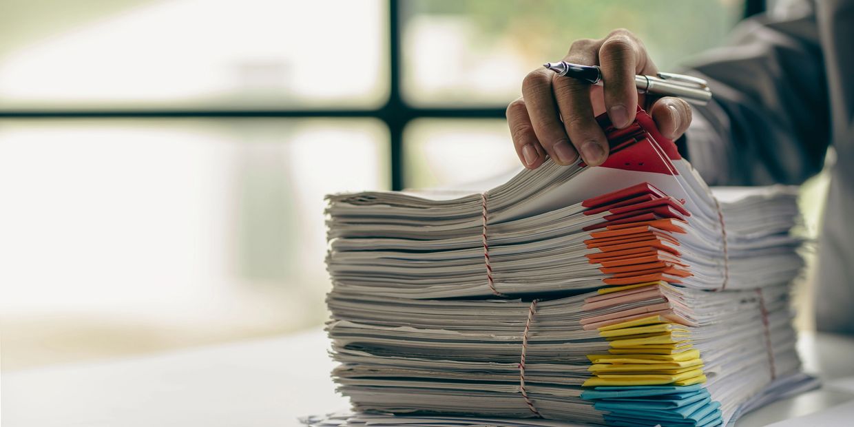 Stacks of organized documents with colorful tabs and a person's hand holding a pen.