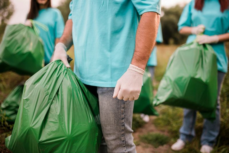 Close up of Spontaneous image of a small group of volunteers with gloves and garbage bags walking through the park they've just cleaned. All wearing jeans and blue t-shirts, being proud and happy for what they did so far, walking and talking, finishing the work