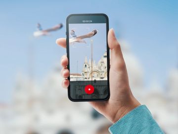 A person records a flying seagull with a smartphone against a historic building.