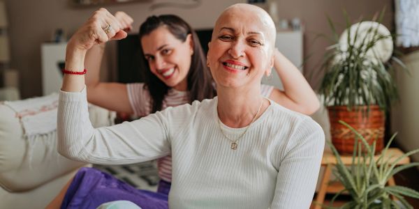 Two women smiling and flexing their arms together indoors.